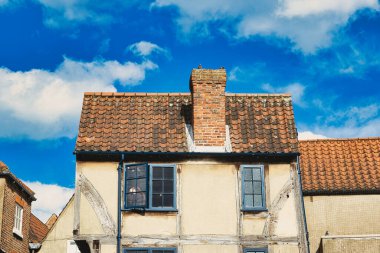 Yıpranmış ön cephesi ve terracotta çatısı olan eski Avrupa binası New York, Kuzey Yorkshire, İngiltere 'de kabarık bulutları olan canlı mavi gökyüzünün arkaplanına karşı..