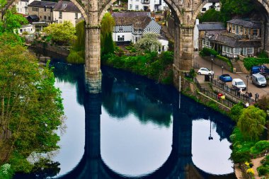 Sakin bir köydeki sakin bir nehrin üzerindeki antik bir taş köprünün havadan görünüşü köprüyü ve çevresindeki yeşilliği yansıtıyor..