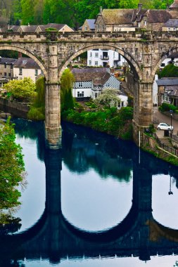 Bereketli yeşillik ve antika evlerle çevrili sakin bir nehrin üzerindeki taş kemer köprü..