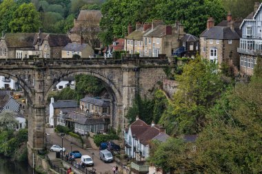 Yeşilliklerle çevrili, üzerinde eski bir taş köprü olan tarihi bir kasabanın manzarası..