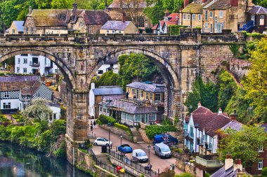 Yeşillik ve geleneksel evlerle çevrili, nehrin üzerinde eski bir taş köprü olan tuhaf bir köy manzarası..