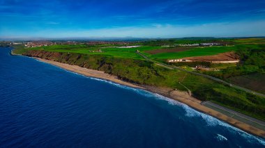 Sahil manzaralı, kumlu bir sahil, yeşil tarlalar ve açık bir gökyüzünün altında mavi bir okyanus..