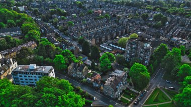 Evlerin, apartmanların ve yemyeşil ağaçların bulunduğu yerleşim yerlerinin hava manzarası. Görüntü, kentsel ve doğal elementlerin bir karışımını yakalayarak bölgenin yerleşim ve yeşilliğini gösteriyor..