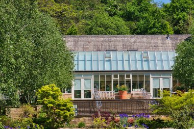 Geniş camdan bir konservatuarı olan modern bir ev yemyeşil ve bakımlı bir bahçeyle çevrili..