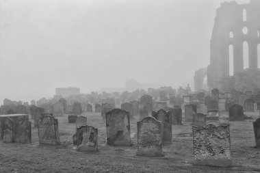 A foggy cemetery with numerous old tombstones and a partially visible ancient ruin in the background. clipart