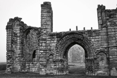 Black and white photo of ancient stone ruins with archways and weathered walls, set against a foggy background. clipart