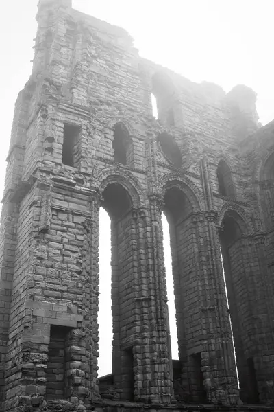 stock image A black and white photograph of an ancient stone ruin with tall arched windows and weathered brickwork. The structure appears to be part of a historical building or castle.