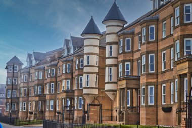 Eşsiz silindirik kuleleri ve sivri çatıları olan bir dizi modern tuğla apartman binası. Binaların önünde birden fazla pencere ve siyah metal çitler var..