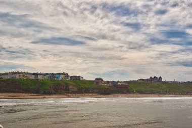 Kıyı kasabası, kumlu bir sahile tepeden bakan binalar ve bulutlu bir gökyüzünün altında okyanus..