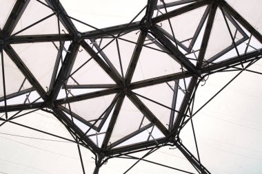 Aşağıdan bakıldığında birbirine bağlı üçgen paneller ve metal desteklerden oluşan karmaşık bir geometrik yapı. Tasarım, şeffaf kaplamalı modern bir mimari tarzını sergiliyor..