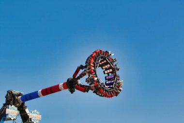 Biniciler için koltukları olan dairesel bir platformda, açık mavi gökyüzüne karşı havada asılı, heyecan verici bir lunapark gezisi. Yolculuk kırmızı, beyaz ve mavi renklerle süslenerek şenlikli bir atmosfer yaratıldı..