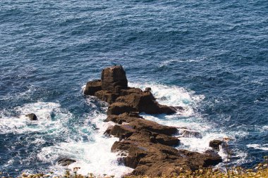 Okyanusta dalgaların çarptığı kayalık bir çıkıntı. Su koyu mavidir, ve manzara kıyı manzaralarının doğal güzelliklerini yakalar..