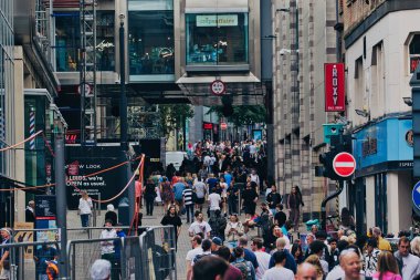 Kalabalık bir sokak, alışveriş yapan ve yürüyen bir sürü insanla dolu. Dükkanlar caddede görünür bir şekilde, hareketli bir atmosfer yaratıyor. Mimaride modern ve geleneksel elementler yer alıyor.