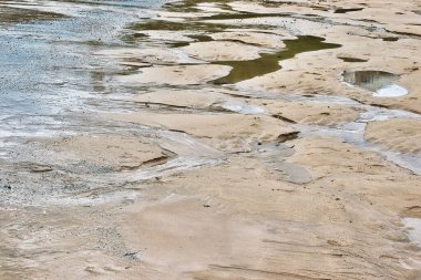 Sığ su havuzları ve yumuşak dalgalarla sakin bir kumsal manzarası. Kum, sakin ve sakin bir atmosferi yansıtan su akışının yarattığı desenlerle desenlenir..