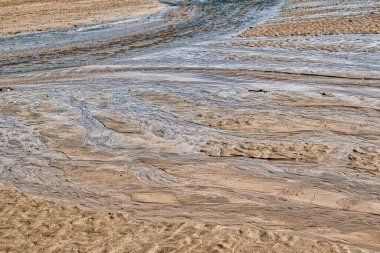 Suyun aktığı kumlu bir sahilin yakından görüntüsü kumda desenler oluşturur. Su berrak görünür ve ışığı yansıtır. Kum ise yumuşak dalgalı pürüzsüz bir dokuya sahiptir. Sahne, bir sahil çevresinin doğal güzelliğini yakalar.