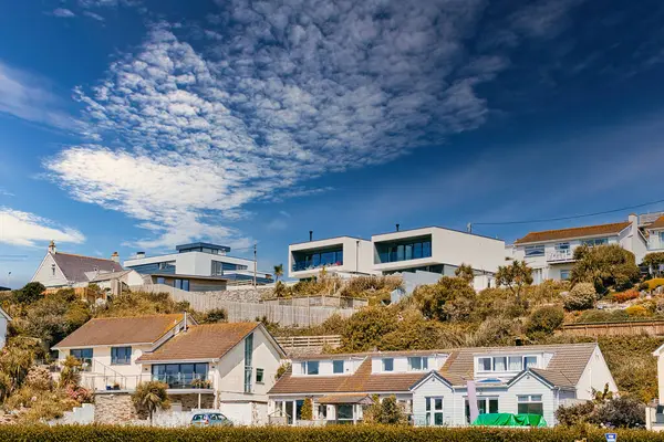 stock image A scenic view of modern houses on a hillside under a partly cloudy sky. The foreground features traditional homes with sloped roofs, while the background showcases contemporary architecture with flat roofs. Lush greenery surrounds the properties, enh