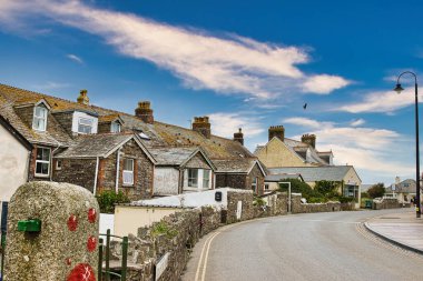 Tahta tavanlı, parlak mavi bulutlu, büyüleyici evlerin yer aldığı pitoresk bir sokak manzarası. Yol yavaşça kıvrılır, taş duvarlar ve yeşilliklerle kaplı, dingin bir atmosfer yaratır..