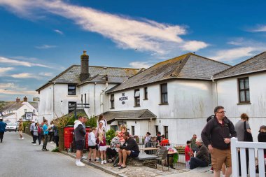 Meyhanenin dışında insanların sokakta ve verandada toplandığı canlı bir sahne. Bina beyaz ve üzerinde 