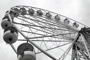 Bulutlu bir gökyüzüne karşı geniş bir dönme dolabın alçak açılı görüntüsü. Yapısı metalik, beyaz kamaralı, modern bir tasarım sergiliyor..