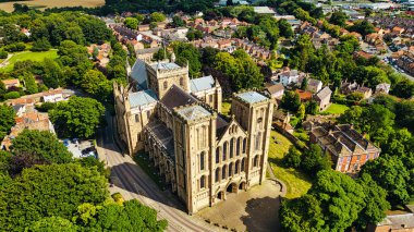 Yeşillik ve konut binalarıyla çevrili büyük, tarihi bir katedralin havadan görünüşü. Katedralde yüksek kuleler ve karmaşık mimari ayrıntılar yer alıyor, bir ağaç zeminine ve küçük bir kasabaya karşı kurulmuş..