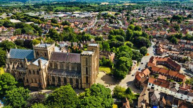 Yeşillik ve yerleşim yerleriyle çevrili tarihi bir katedralin havadan görünüşü. Katedral, geniş bir yapısı ve birden fazla kulesi olan karmaşık bir mimariye sahiptir. Yakınlarda, kırmızı çatıları ve manzarası olan antika evler var.