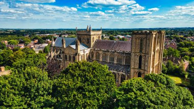 Yeşillik ve manzarayla çevrili tarihi bir katedralin havadan görünüşü. Gökyüzü kabarık bulutlarla parlıyor, ve şehir arka planda görünüyor, doğa ve mimarinin bir karışımını sergiliyor..