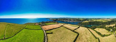 Bereketli yeşil tarlaların, bir nehrin ve açık mavi gökyüzünün altındaki uzak bir kasabanın bulunduğu panoramik bir kıyı manzarası..