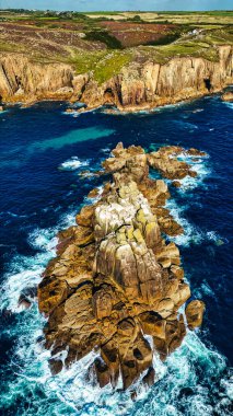 Dalgaların kayalara çarptığı kayalık bir kıyı şeridinin havadan görüntüsü. Manzara, engebeli uçurumlar ve canlı mavi okyanus sularını barındırıyor ve kıyı çevresinin doğal güzelliklerini gözler önüne seriyor..