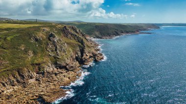 A stunning aerial view of rugged cliffs along a coastline, with clear blue waters and a bright sky. The landscape features green hills and rocky shorelines, showcasing the natural beauty of the area. clipart