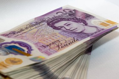 Queen 'lerin portresinin en üstte göründüğü bir yığın İngiliz banknotunun yakın çekimi. Banknotlar düzenli bir şekilde düzenlenmiş..