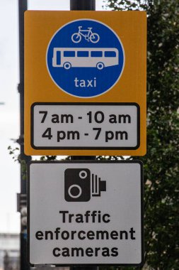 Belirli çalışma saatleri ve trafik kameraları olan bir otobüs ve taksi şeridini gösteren trafik işareti..