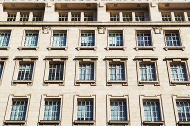 Dekoratif çerçevelerde tekrar eden pencere desenli bir bina cephesinin yakın çekimi. Pencereler Manchester, İngiltere 'de açık renkli taştan bir duvar ve dekoratif detaylarla düzenlenmiş..