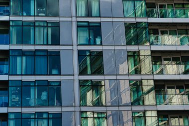 Birden fazla pencere ve balkonları olan modern cam bir binanın yakın çekimi. Pencereler Manchester, İngiltere 'de mavi ve yeşil renkli bir desen oluşturarak çevre şehri yansıtıyor..