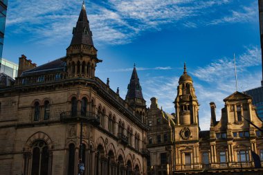 Manchester, İngiltere 'de beyaz bulutlu parlak mavi gökyüzüne karşı birkaç süslü taş bina ve karmaşık detaylar içeren alçak açılı bir çekim..