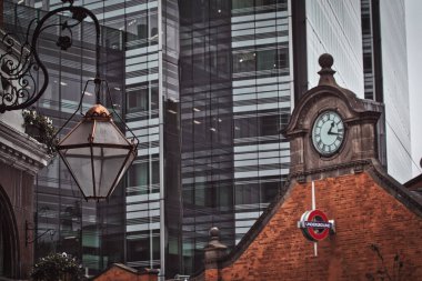 Modern bir gökdelenin önünde asılı bir fener, saat kulesi olan kırmızı tuğlalı bir bina ve ön planda 