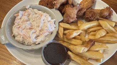 Kızarmış tavuk kanadı, patates kızartması, küçük bir kasede lahana salatası ve küçük bir kutu kara sos içeren beyaz bir tabak..