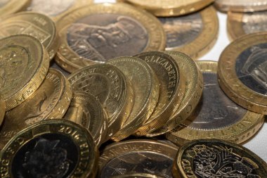 İngiliz 1 poundluk bozuk paralarının yakın plan görüntüsü, çeşitli tasarımları ve yılları gösteriyor. Bozuk paralar, daha koyu merkezleri olan altın renginde, aşınma ve yırtık gösteriyor. Rastgele dizilmişler, bazıları üst üste dizilmiş..