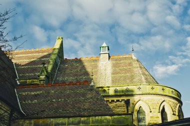 Binanın çatısının bir bölümünde farklı çatı bölümleri, taş işçiliği ve küçük bir kubbe de dahil olmak üzere mimari ayrıntılar yer alıyor. Çatı öncelikle koyu kahverengi / yeşil taş aksanlı fayanslardan oluşur. Gökyüzü kısmen bulutlu.