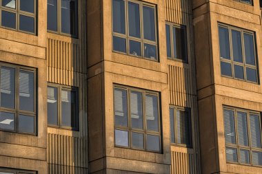 Close-up view of a tan-colored building's exterior, showcasing multiple windows with varying configurations, some with blinds.  The building's facade features vertical linear detailing. clipart