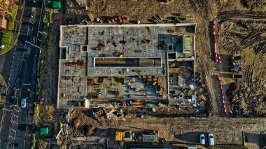 İnşaat halindeki bir binanın havadan görüntüsü. İnşaat malzemeleri ve toprak işleriyle çevrili büyük bir beton levha merkeze hakim. Bölgenin yakınlarında araçlar görülüyor..