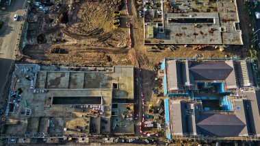 İnşaat halindeki iki binanın havadan görüntüsü. Birinde beton tabanlı, diğerinde koyu gri çatılı, kazılmış toprak ve inşaat malzemeleriyle çevrili..