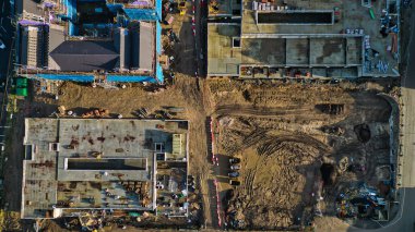 İnşaat alanının hava görüntüsü kısmen tamamlanmış iki bina, açık toprak ve inşaat ekipmanları gösteriyor. Arazi çamurlu raylar ve bariyerlerle bölünmüş..