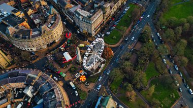 Aerial view of a city square featuring a Ferris wheel, surrounding buildings, parked cars, and a Christmas market. The scene is captured during the day, showing a mix of architectural styles and urban landscaping. clipart