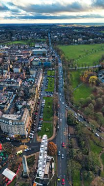 Bir şehir merkezinin havadan görünüşü, bir dönme dolap, park edilmiş arabaların olduğu bir ana yol, konut binaları, ağaçlı bir park, ve bir anıt..