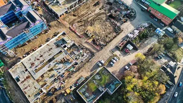 İnşaat halindeki binaları, kazılmış arazileri, park edilmiş araçları ve çevresindeki yeşillikleri gösteren hava manzarası. Tamamlamanın çeşitli aşamalarında birden fazla yapı görünür..