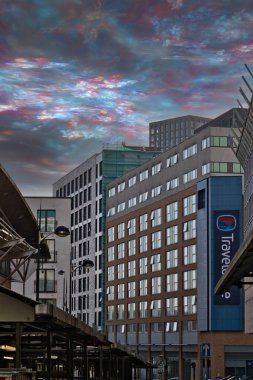 Modern city buildings under a vibrant, colorful sky.  A Travelodge sign is visible on one building.  The image features architectural details and a transit structure in Birmingham, UK. clipart