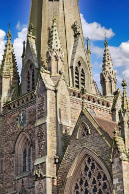 Close-up view of a church steeple's intricate stonework, featuring a clock, arched windows, and ornate detailing against a blue sky in Birmingham, UK. clipart