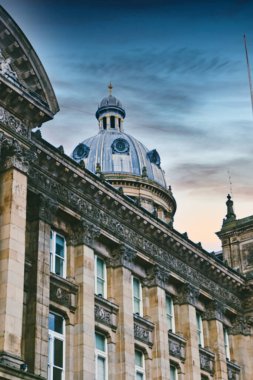 Gösterişli detaylarıyla büyük bir taş binanın alçak açılı görüntüsü alacakaranlık gökyüzünün altında belirgin mavi bir kubbe barındırıyor. Binanın ön cephesi Birmingham, İngiltere 'deki sütunlar, pencereler ve dekoratif taş işleriyle detaylandırılmıştır..