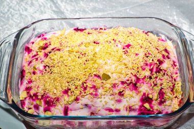 Cam bir fırın tabağı kremalı, pembe tabanlı ve üzerinde dilimlenmiş sarı peynir bulunan katmanlı bir salata içerir. Salata dikdörtgen cam bir tabakta sunuluyor. Görüntü iyi aydınlatılmış ve yemeğin dokusunu ve rengini açıkça gösteriyor, Rus yemeği..