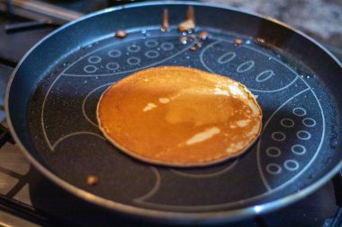 Tek bir altın sarısı krep soba tepsisinde koyu renkli, yapışmaz tavada pişer. Tavanın dekoratif bir deseni var. Yağ kalıntısı görünür..